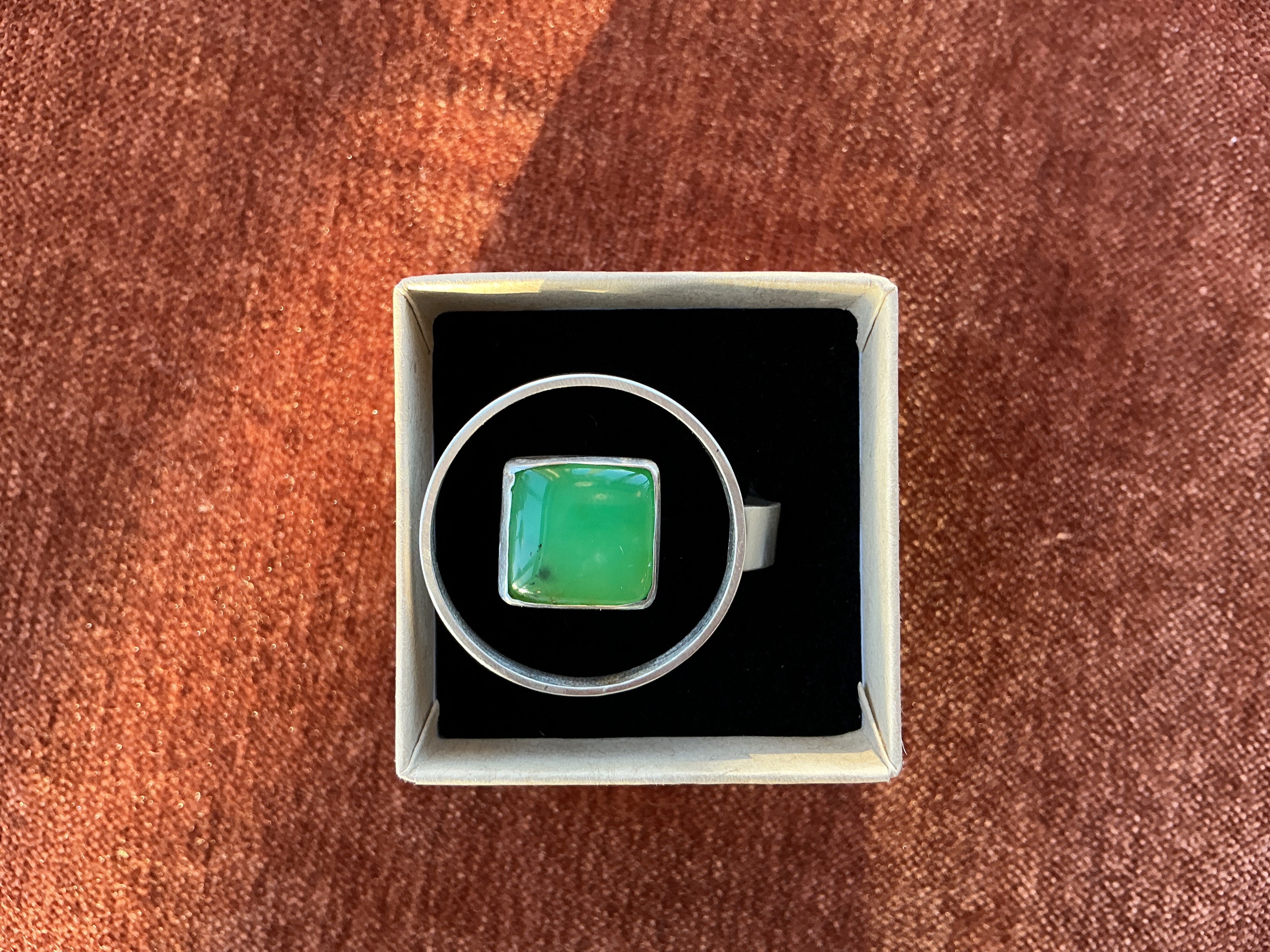 Ring with green gemstone in a box on a brown surface