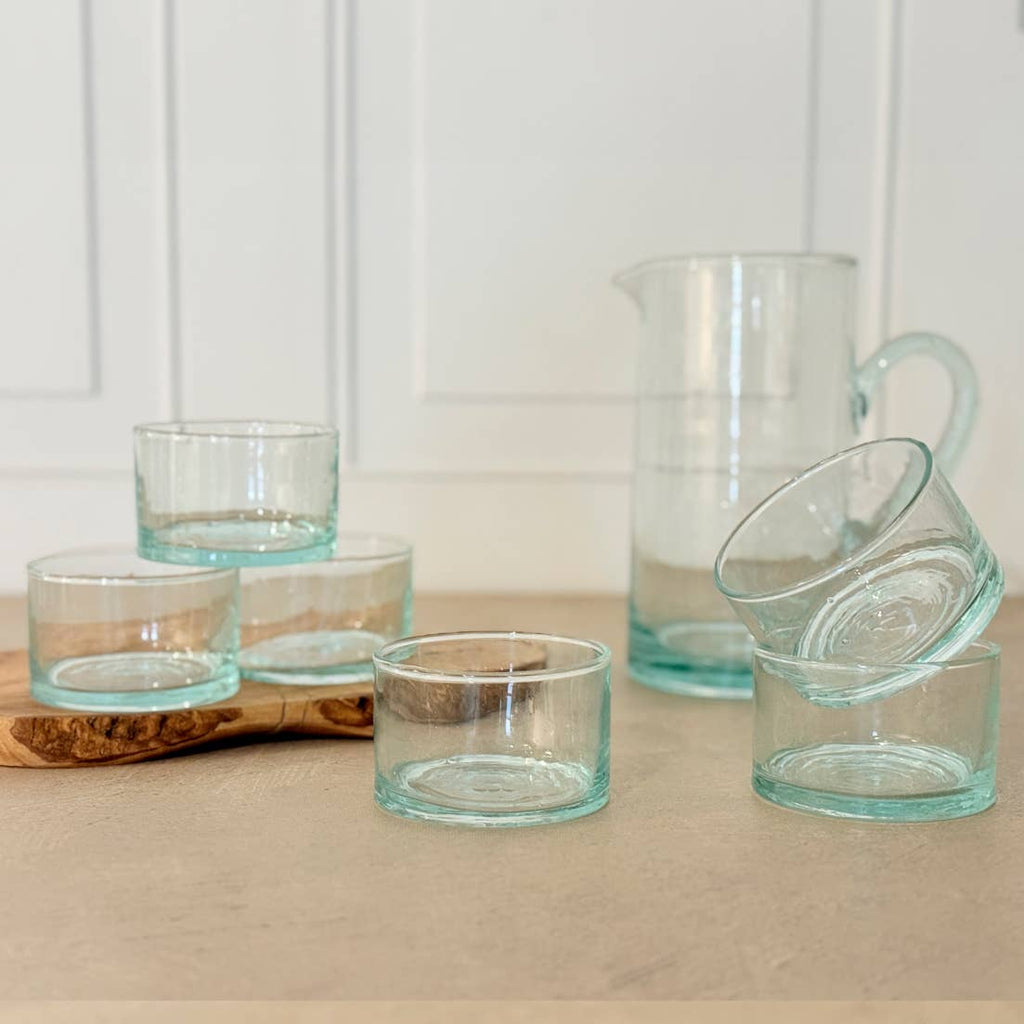 Set of clear glass tumblers and a pitcher on a wooden surface with a white background
