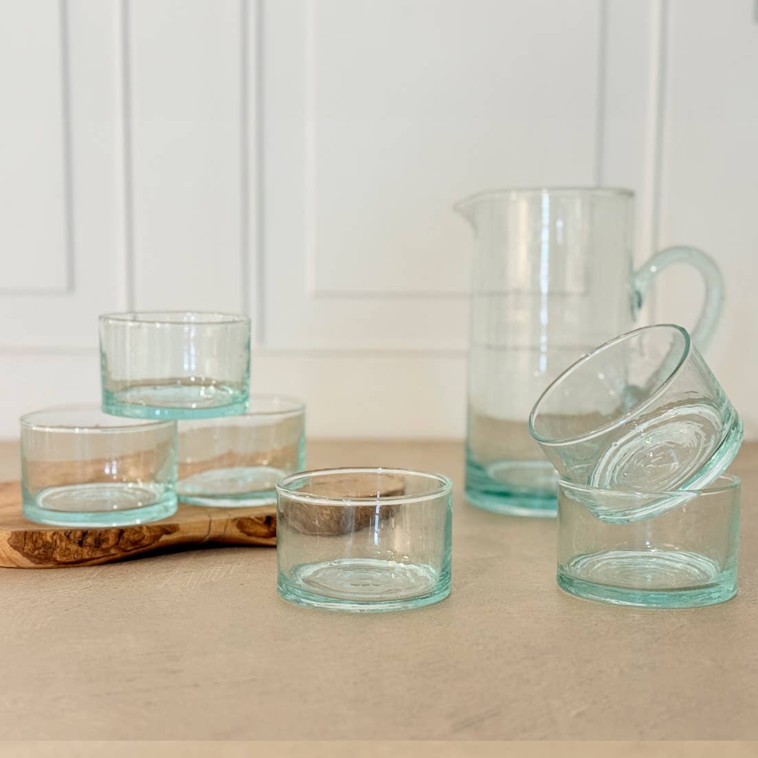 Set of clear glass tumblers and a pitcher on a wooden surface with a white background